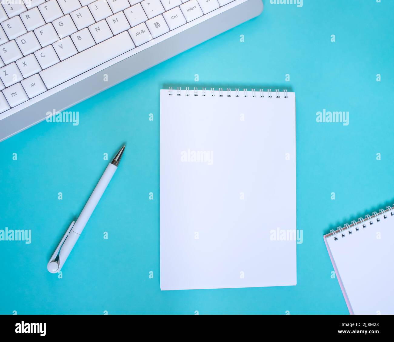 An empty notepad with a pen is on a blue background with a laptop and supplies. Top view with copy space, flat lay. Stock Photo