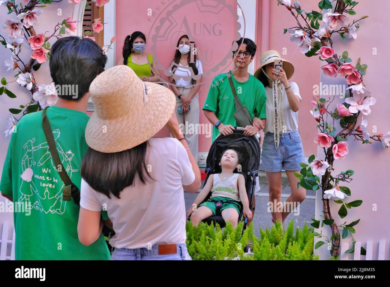 Young Asian tourists pose for selfies at a one-way mirror window of Aung Ku Cafe in Soi Rommanee in the Old Town area of Phuket Town, Thailand Stock Photo
