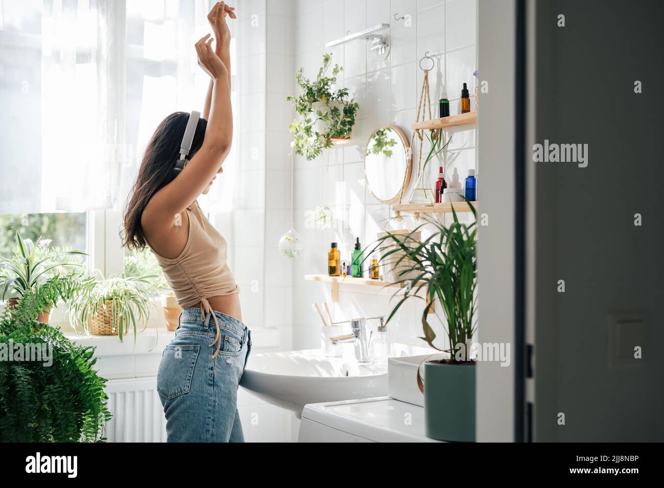 Young hispanic woman dancing with headphones in bathroom. Body positivity, confort hime zone, wellness and lifestyle Stock Photo