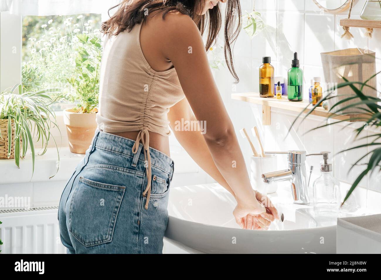 Unrecognisble woman with dark skin washing hands in light bathroom. Natural cosmetics, slef care and wellness concept Stock Photo