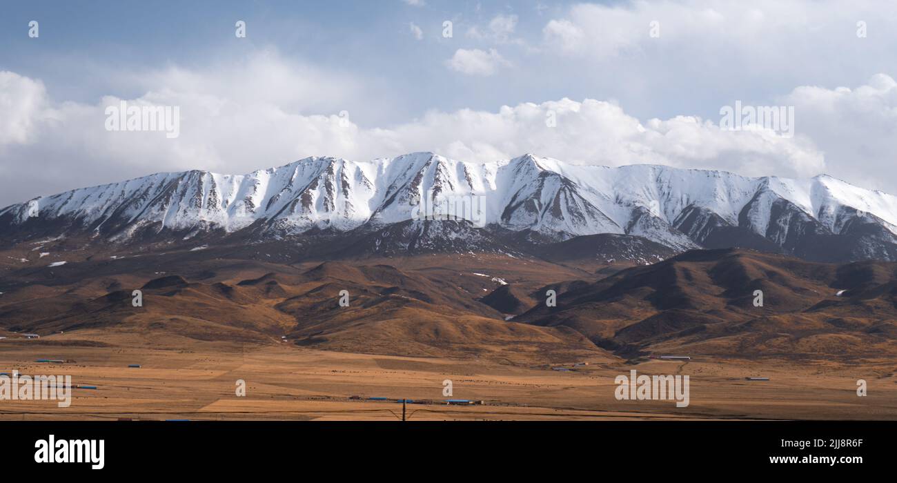 A distant view of the Qilian Mountain range covered in snow in China Stock Photo