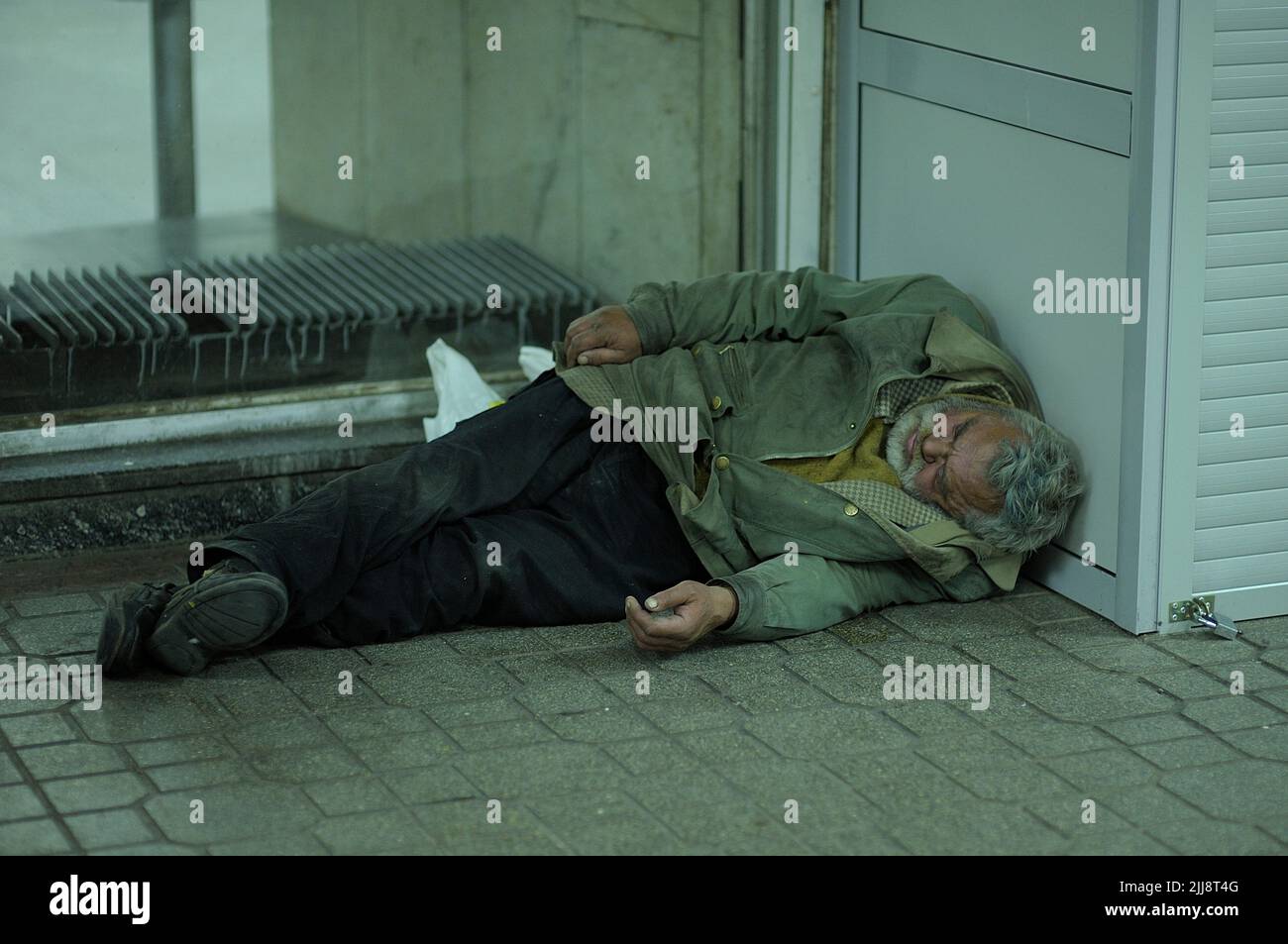 Old homeless man in ragged dirty clothes sleeping on a cold pavement of a subway passage. October 31, 2012. Kyiv, Ukraine Stock Photo