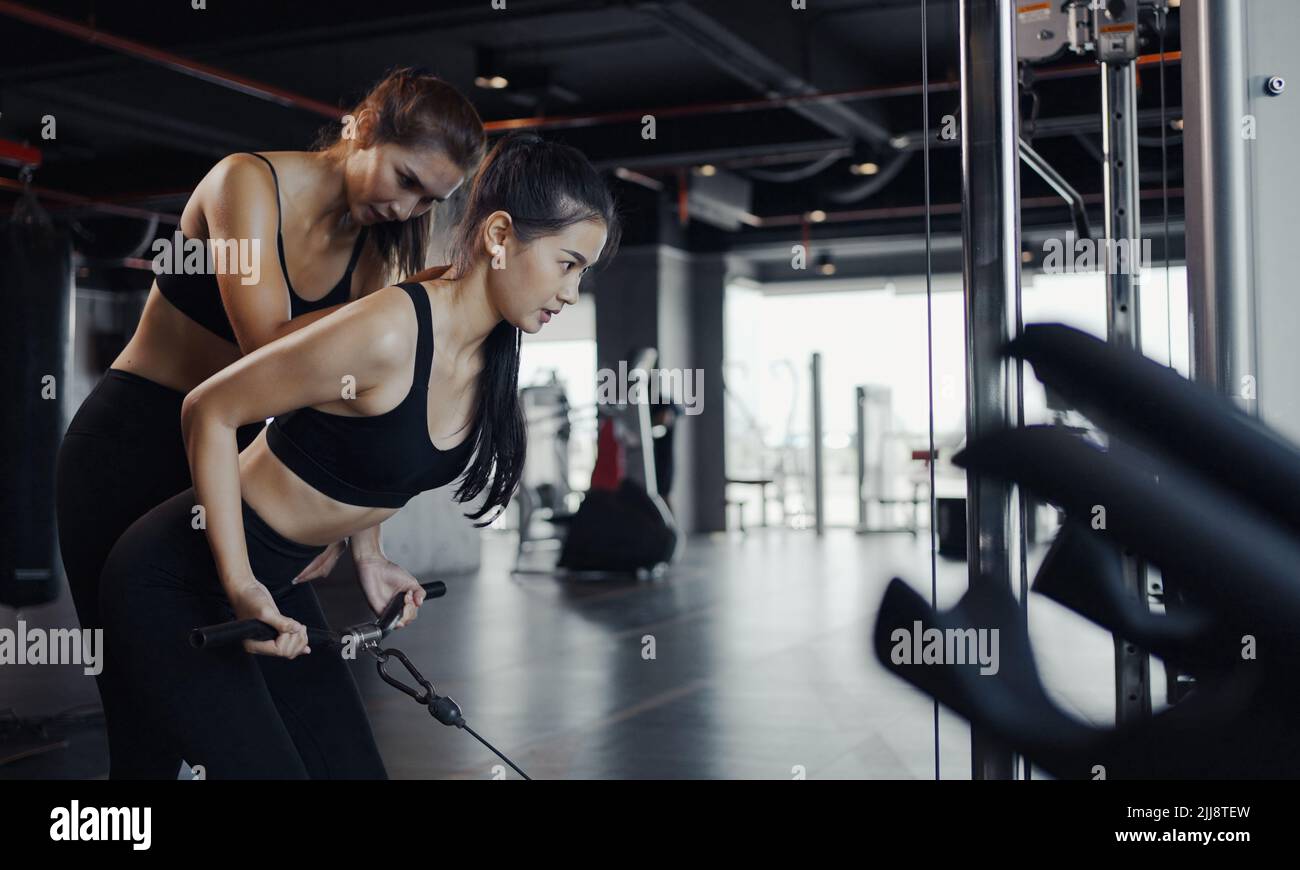 Sporty girl doing weight exercises with the help of her personal trainer at the gym. Stock Photo