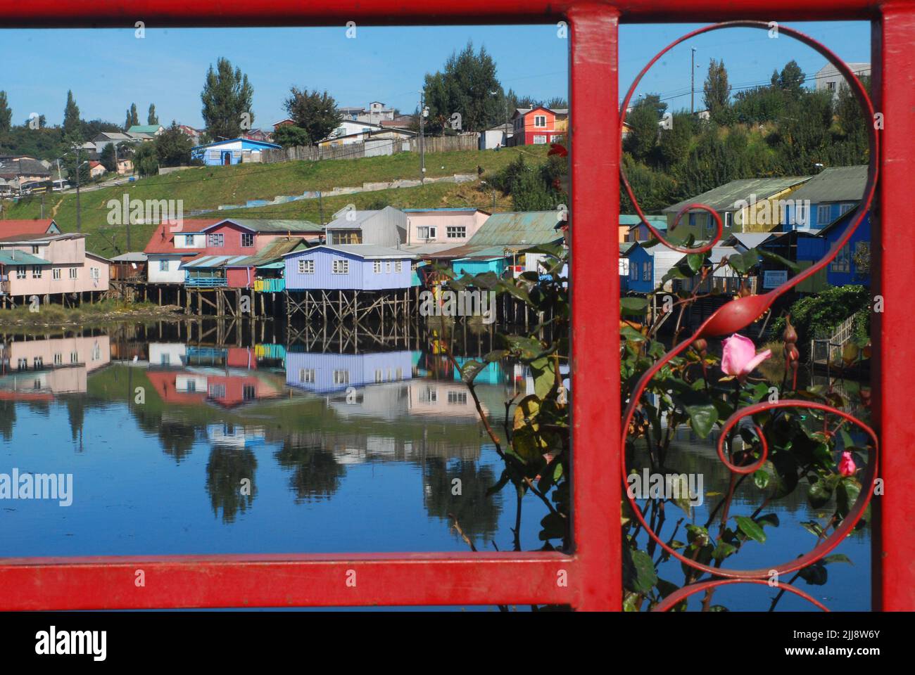 View of the Castro pilings in Chiloe Island, Chile, reflecting on the water through the protective railing of a bridge. Selective focus. Stock Photo