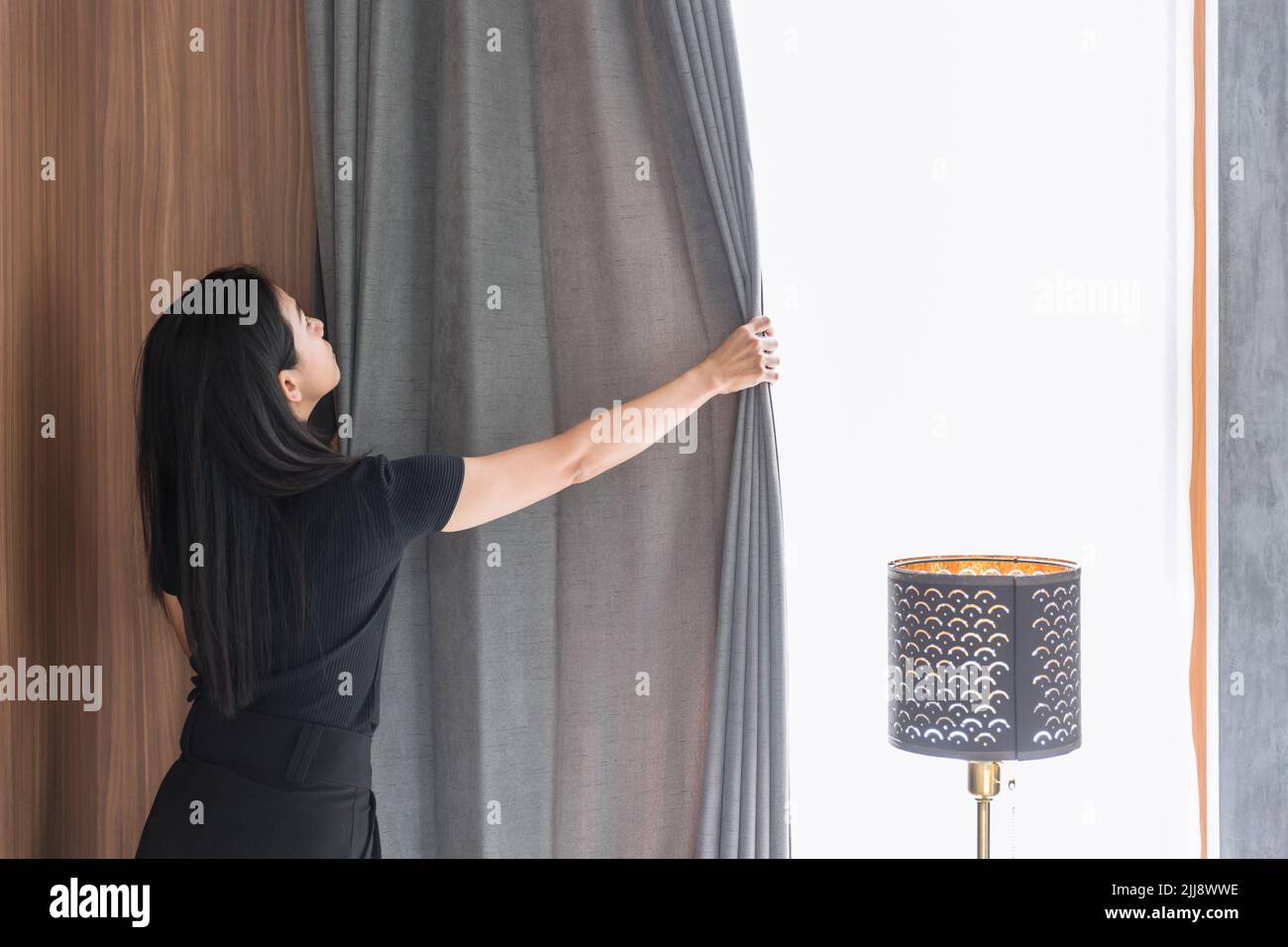 Maid housewife woman working chores housekeeping cleaning room arrange window curtains at home or hotel. Stock Photo