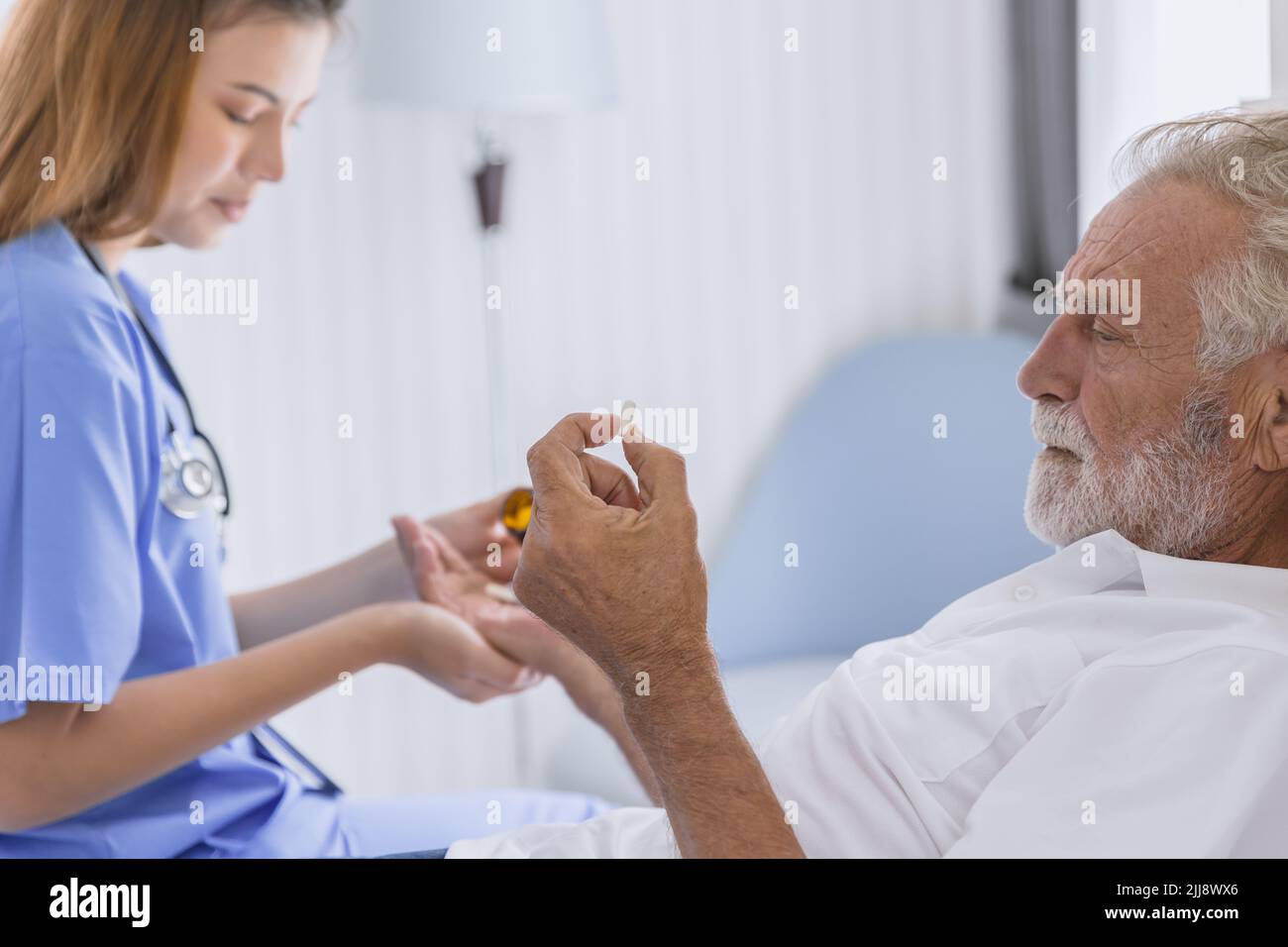 nurse doctor elder healthcare give medicine pill to mental sick stress senior man lay on bed at hospital home care. Stock Photo