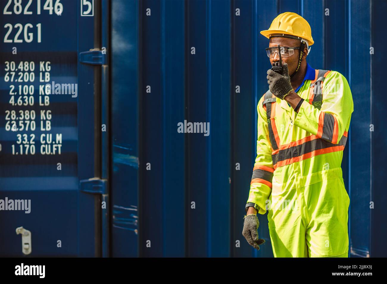 Black African male worker work as port cargo manager using radio control loading container in logistic industry. Stock Photo