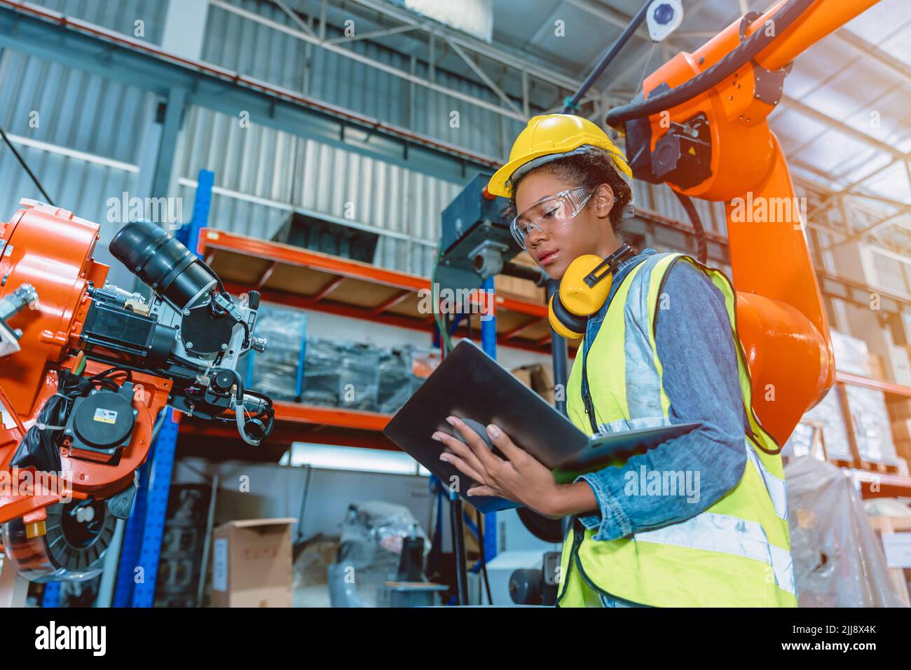 Engineer smart woman worker working programing robotic welding machine. Black teen girl work in advance modern factory. Stock Photo