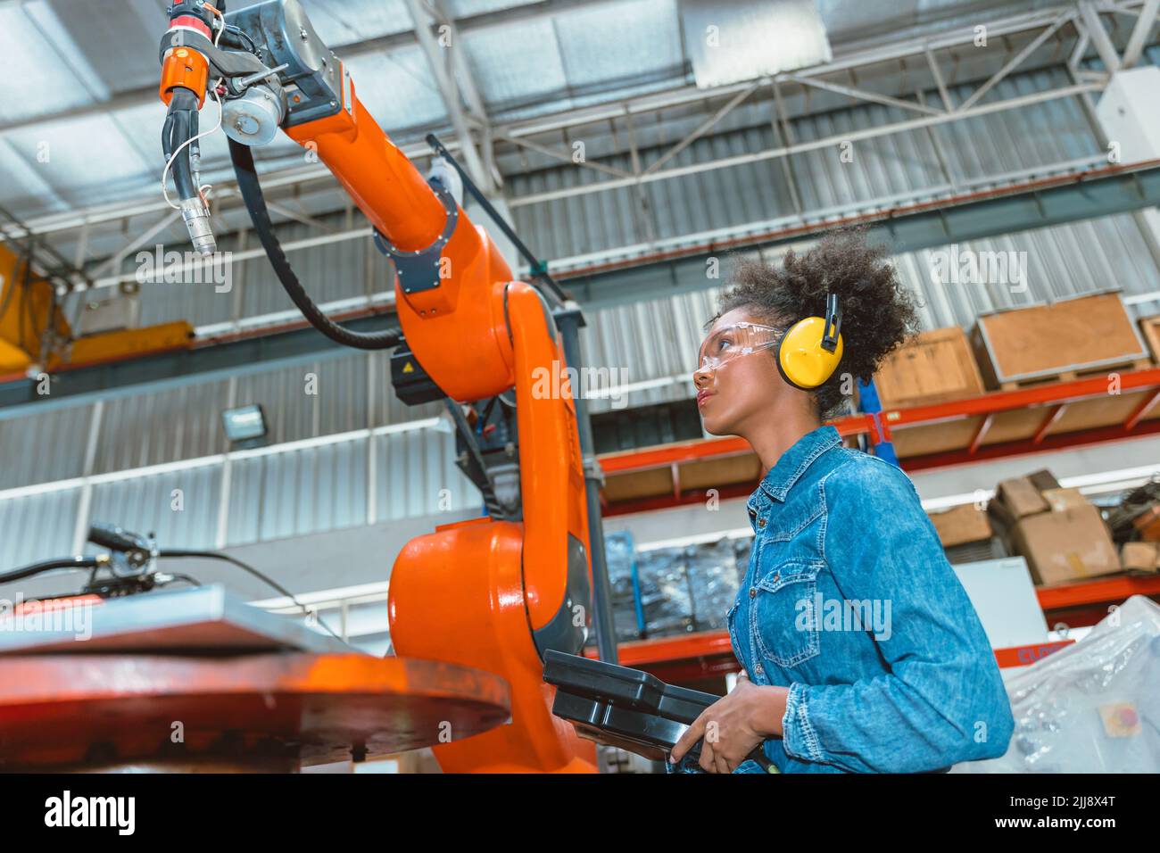 Engineer smart woman worker working programing robotic welding machine. Black teen girl work in advance modern factory. Stock Photo