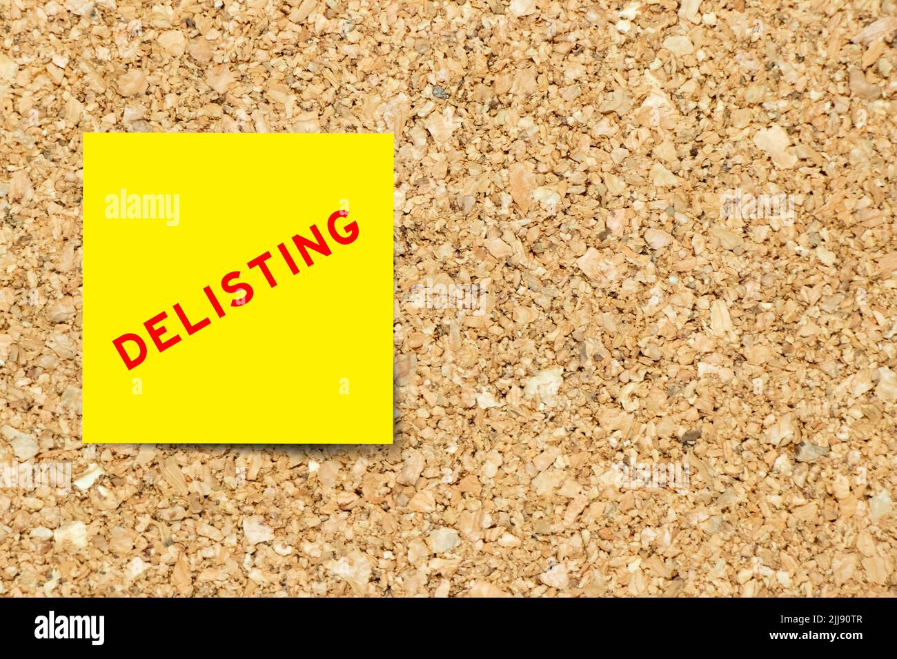 Yellow note paper with word delisting on cork board background with copy space Stock Photo