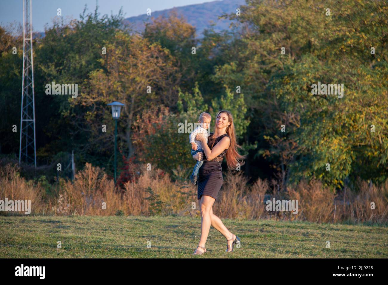 Loving young mother walking and carring her toddler son in hands outdoors on autumn walk Stock Photo