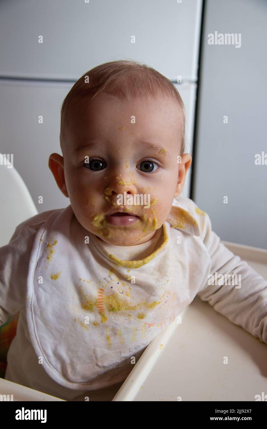 Portrait of messy and dirty baby eating food, little boy learning to