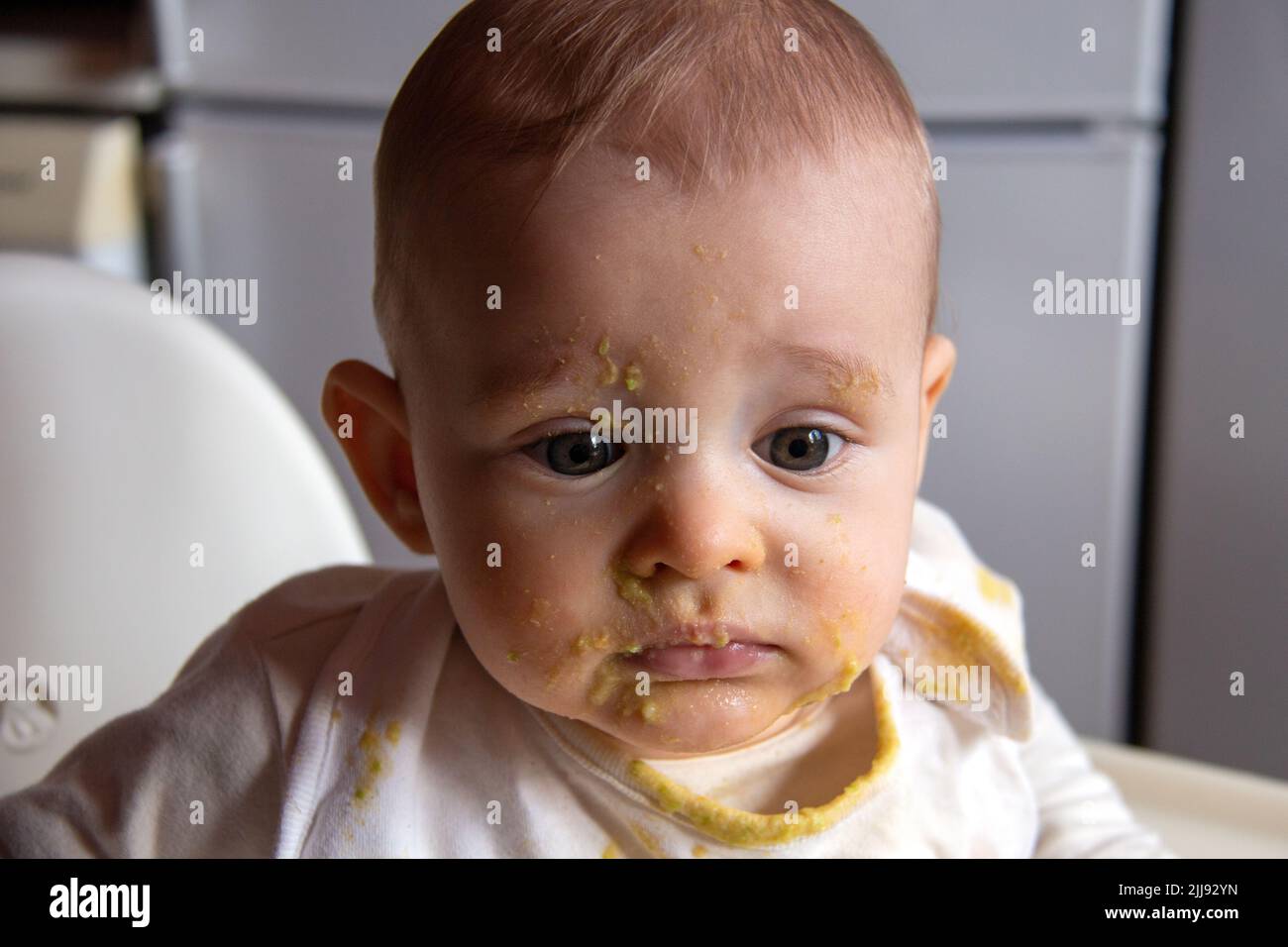 Portrait of messy and dirty baby eating food, little boy learning to