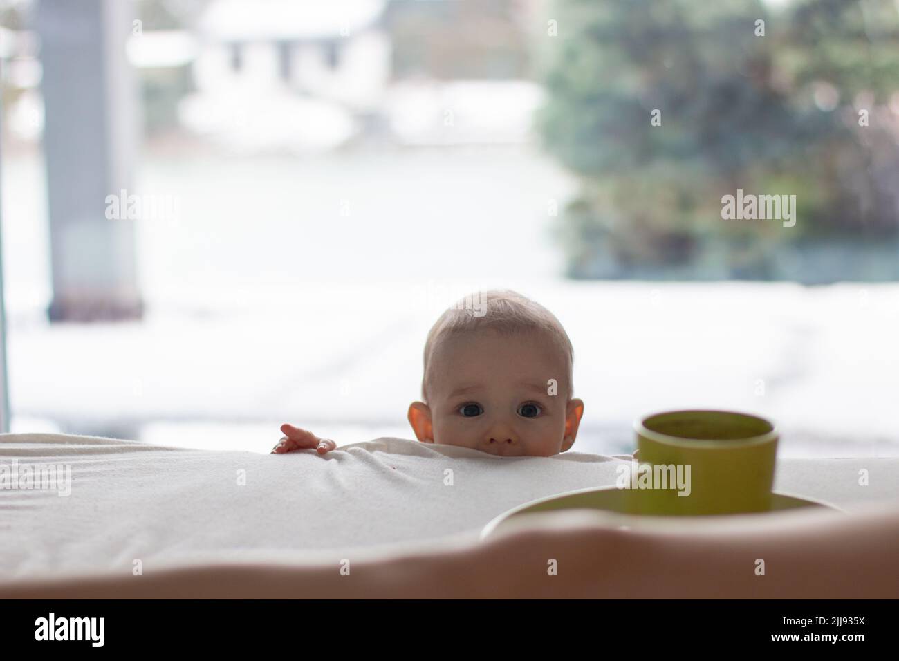 Curious child toddler wants to do mischief and is watching up to parents bed to hot coffee cup, home scene copy space background Stock Photo