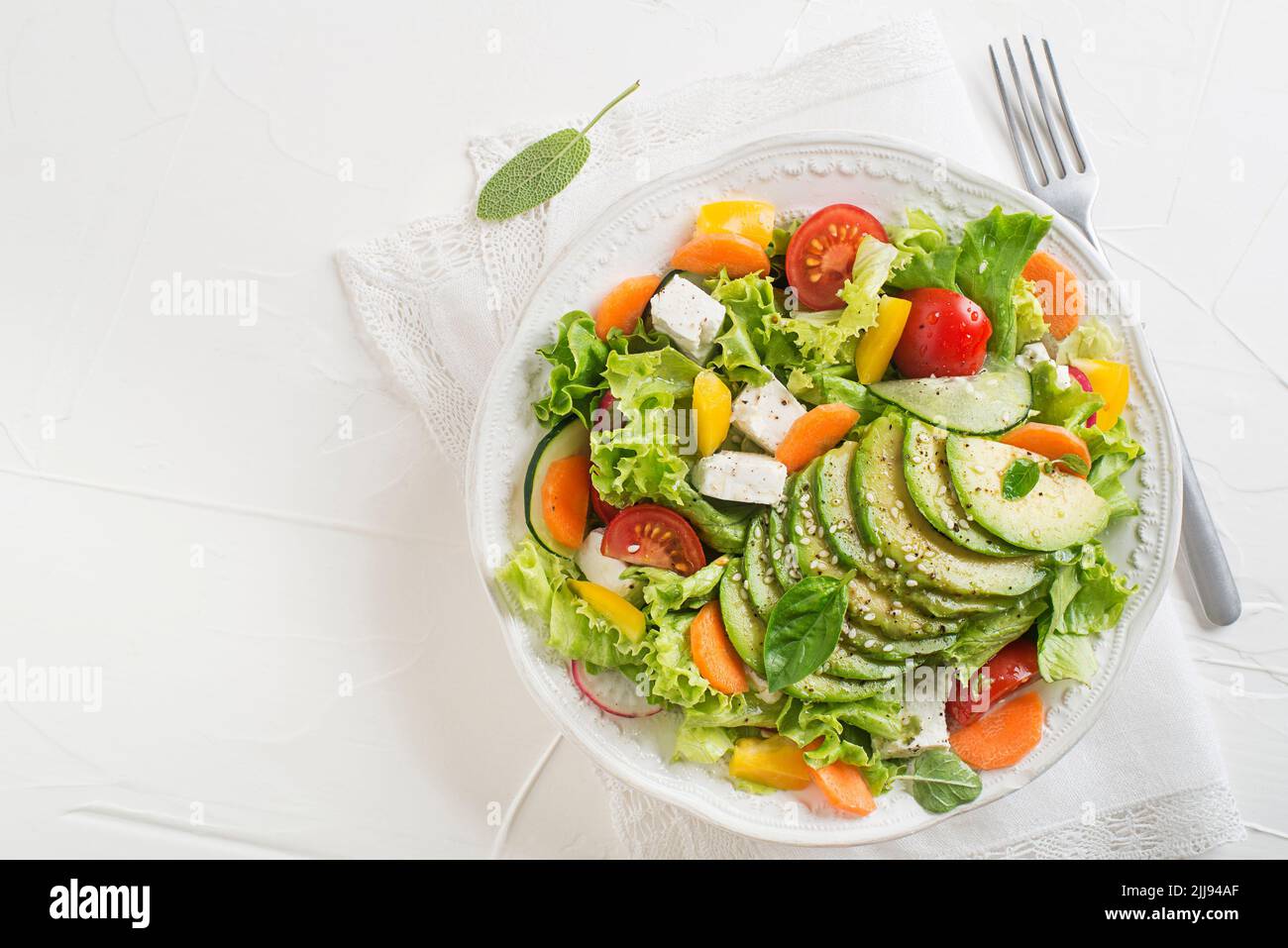 Healthy green salad with avocado, feta cheese and fresh vegetables on white background close up Stock Photo