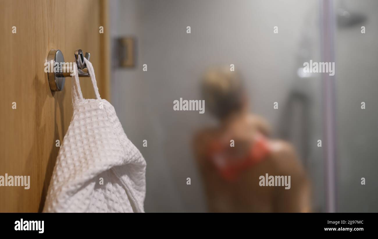White bathrobe on hook and woman in shower in background Stock Photo