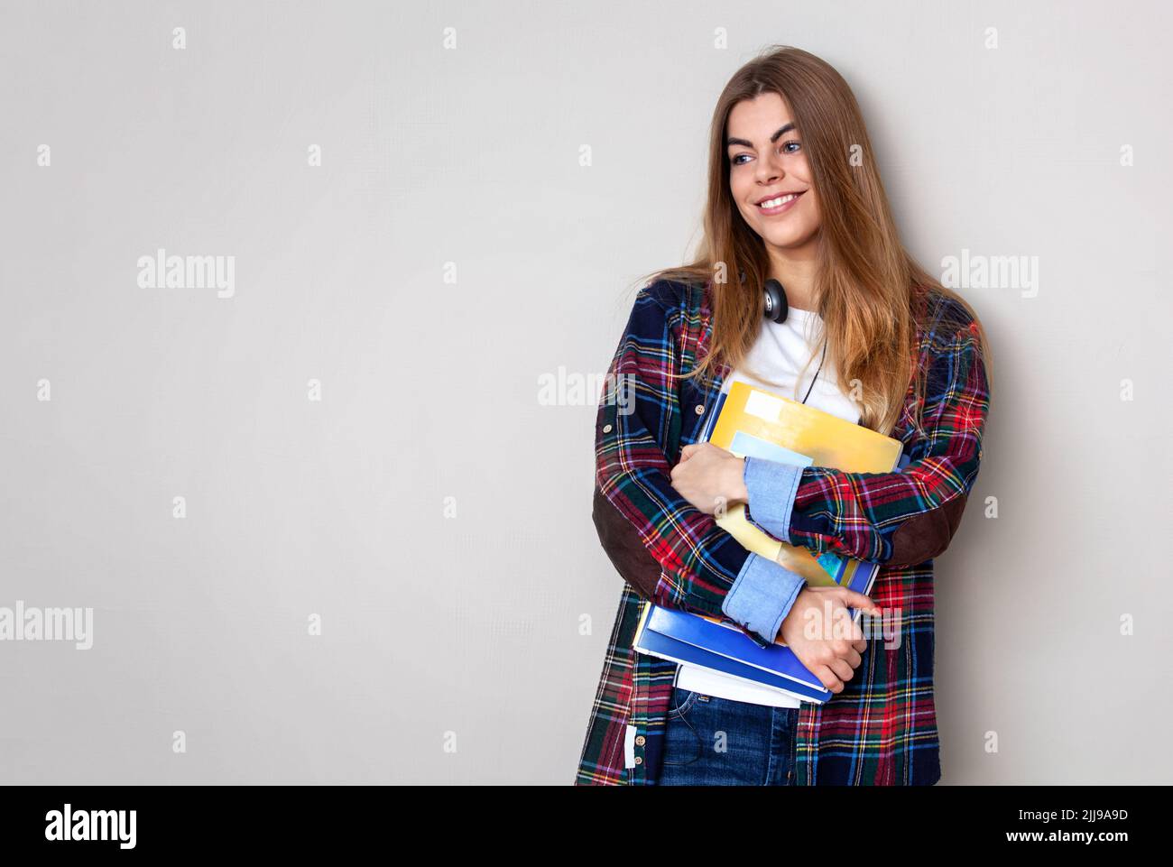 Studio portrait of young beautiful female student with books standing against wall. Stock Photo