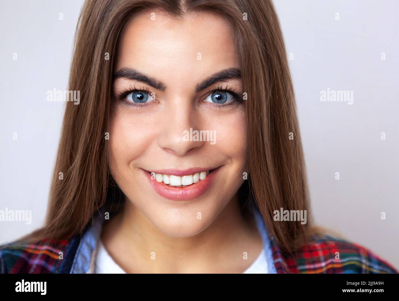 Studio portrait of happy young woman in plaid shirt posing against wall. Stock Photo