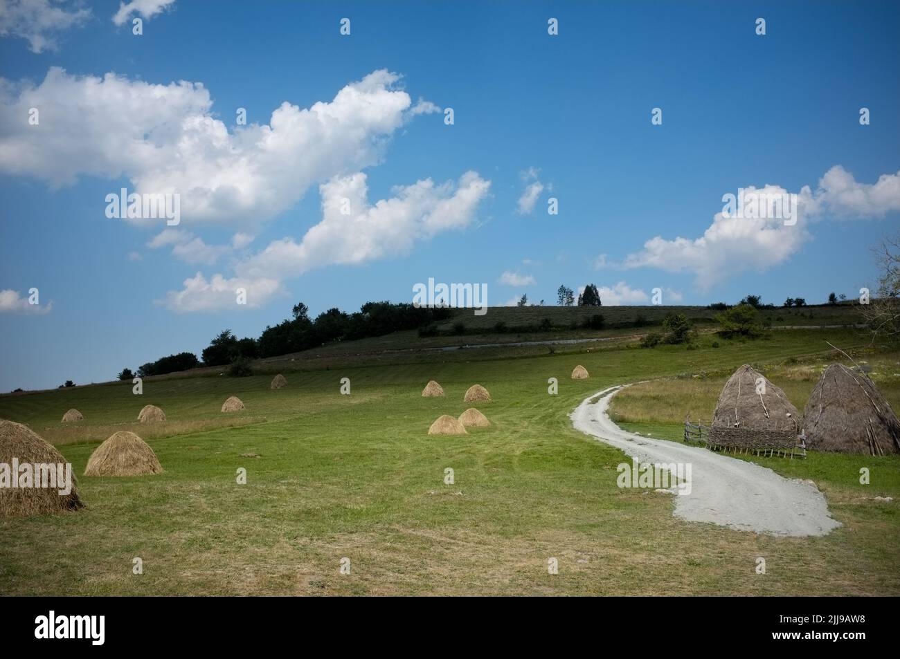 clouds sky on haystacks in a meadow of Serbia with winding path Stock Photo