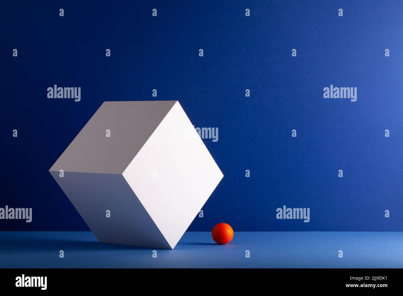 White cube with orange golf ball on the blue background. Creative image. Stock Photo