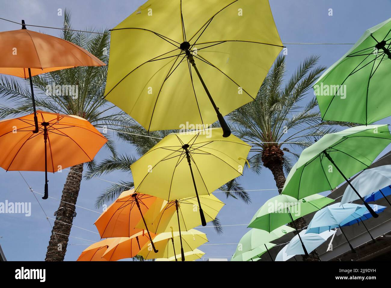 A group of different colored umbrellas hang overhead a walkway. Stock Photo