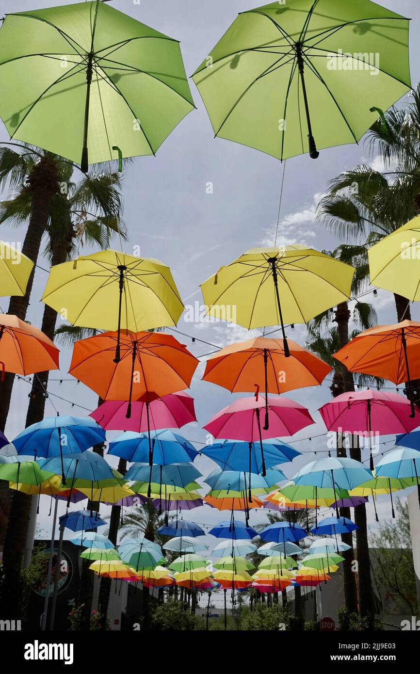 A group of different colored umbrellas hang overhead a walkway. Stock Photo