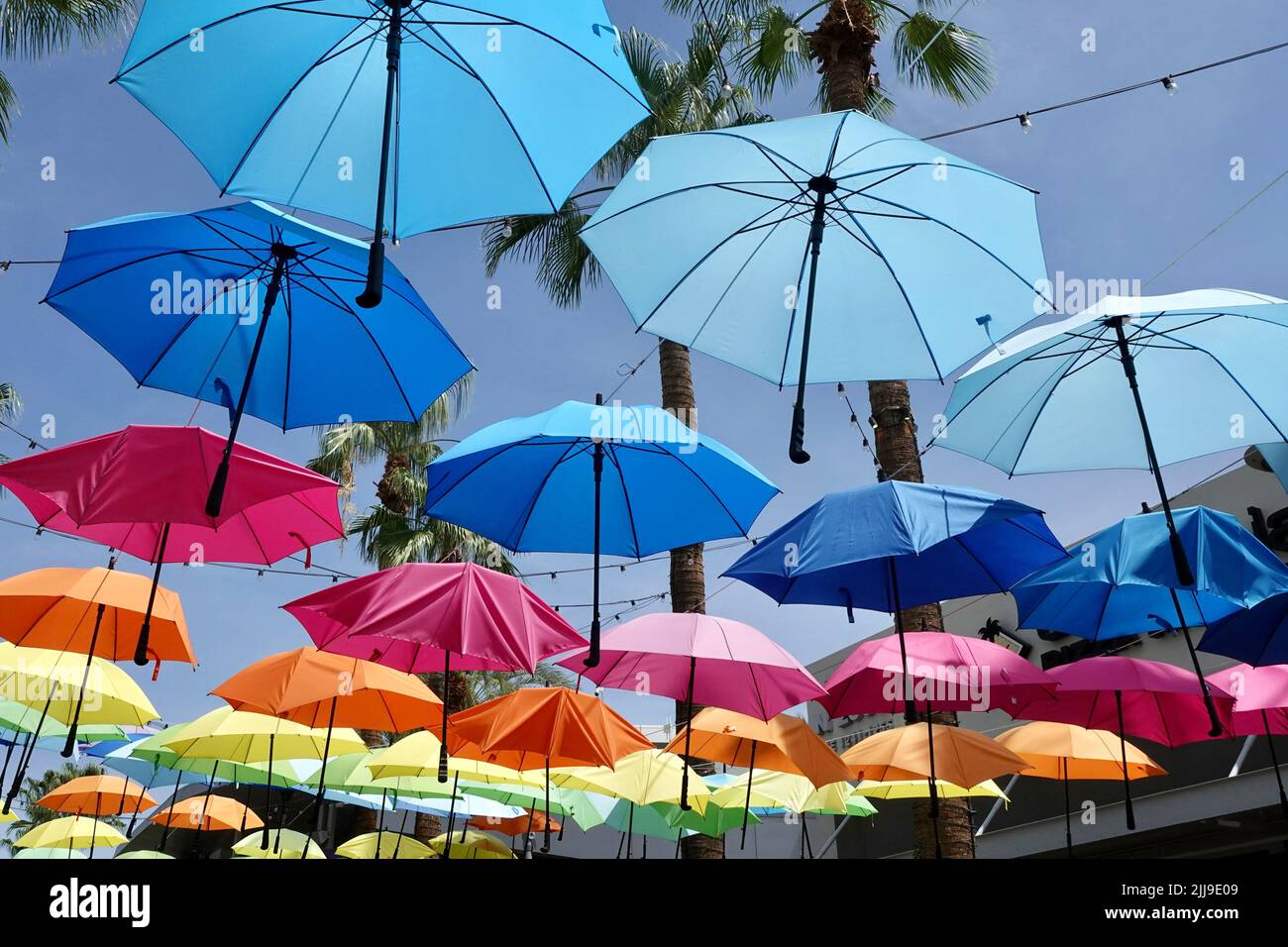 A group of different colored umbrellas hang overhead a walkway Stock