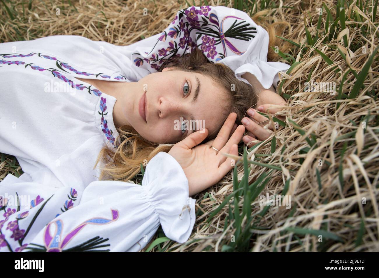 portrait of a beautiful Ukrainian girl 17-19 years old in an embroidered traditional blouse lies on dry grass. view from above. Pride to be Ukrainian. Stock Photo