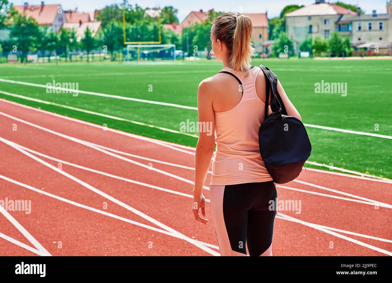 Back view of girl with sport bag at stadium track, Woman going on fitness training at summer day Stock Photo