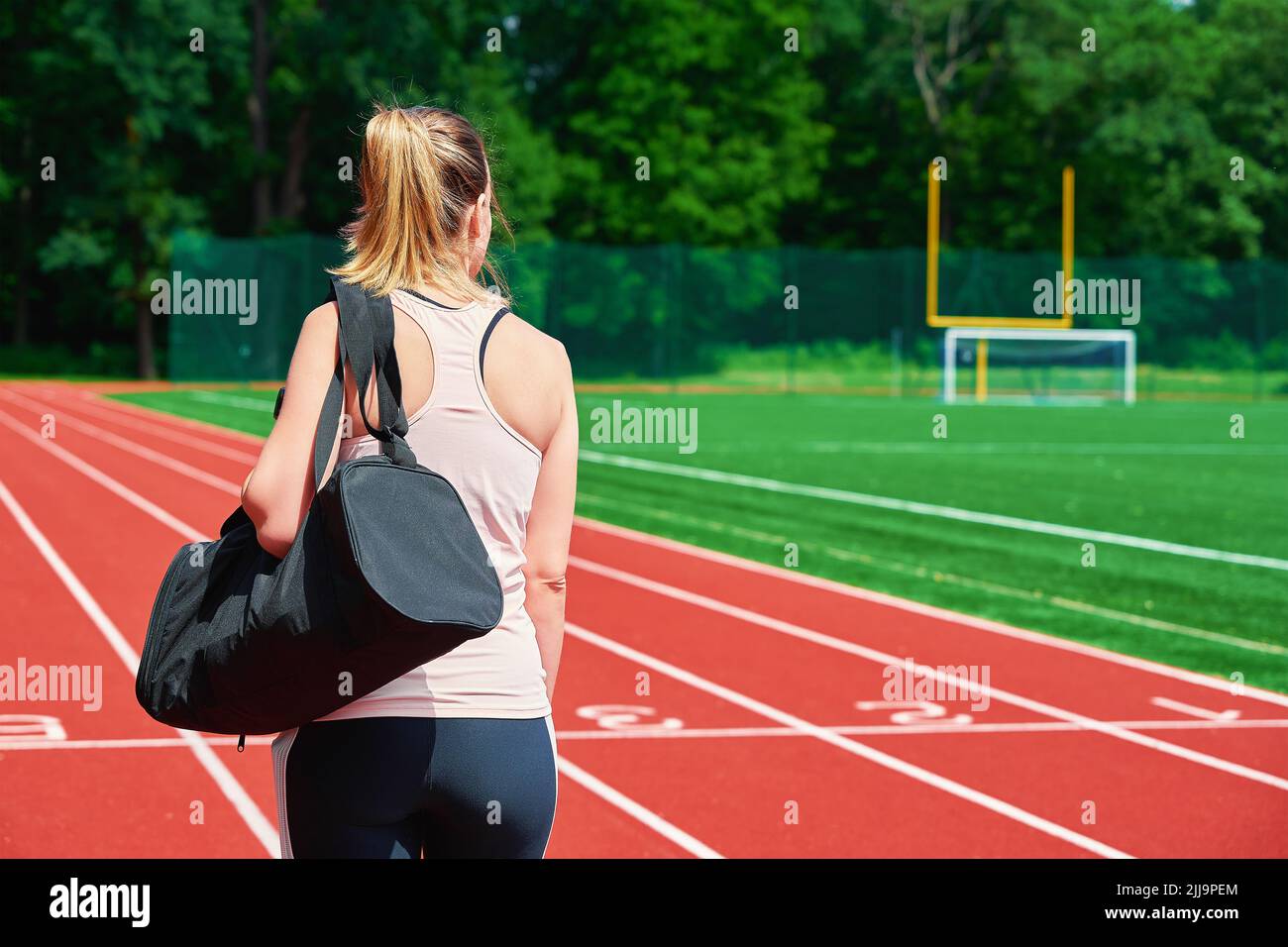 Back view of girl with sport bag at stadium track, Woman going on fitness training at summer day Stock Photo