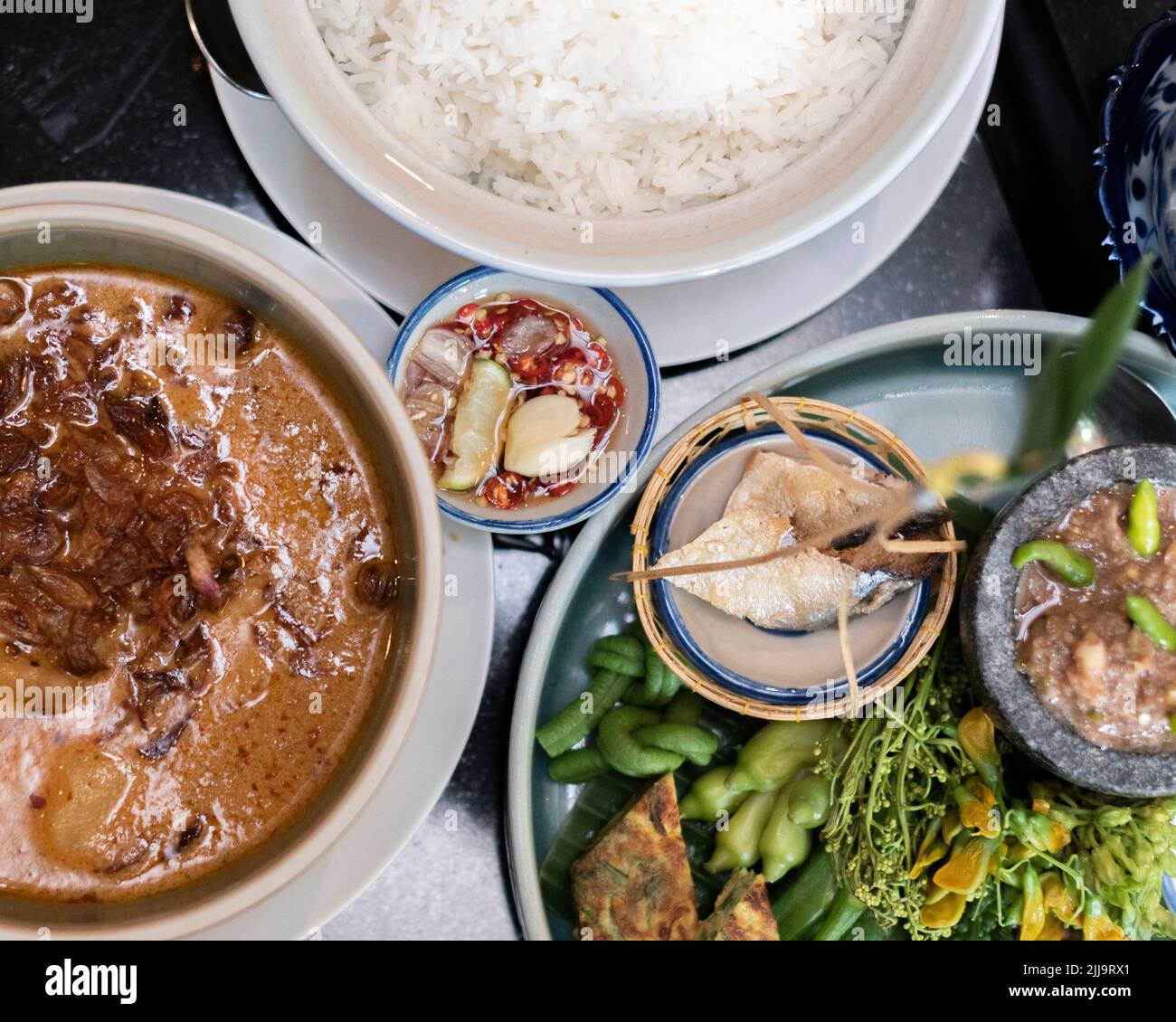 A top view of various Thai dishes in bowls set on a dark marble table ...