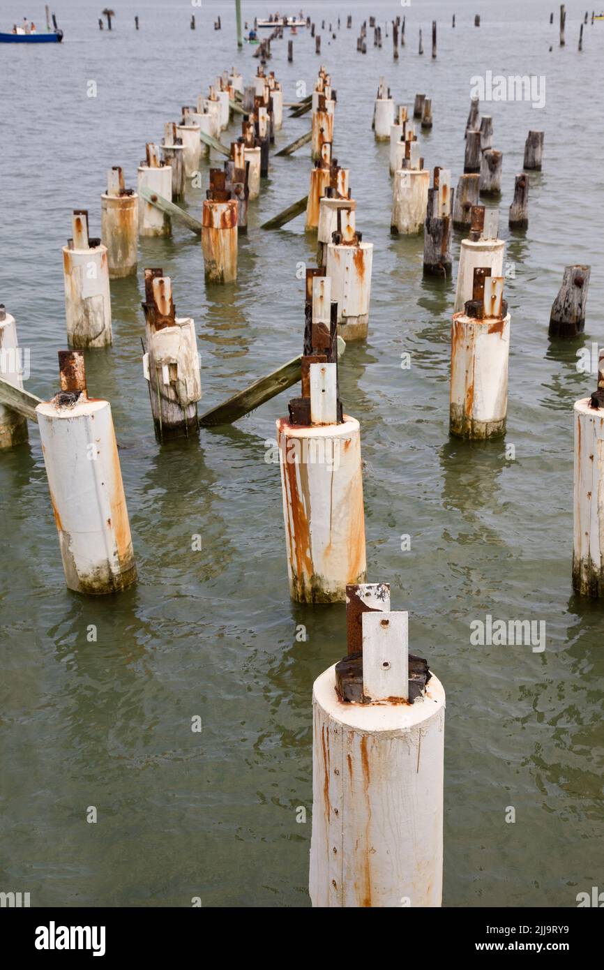 Deteriorated old pier pilings with small boats in the background at the shoreline of Delaware Bay USA. Stock Photo
