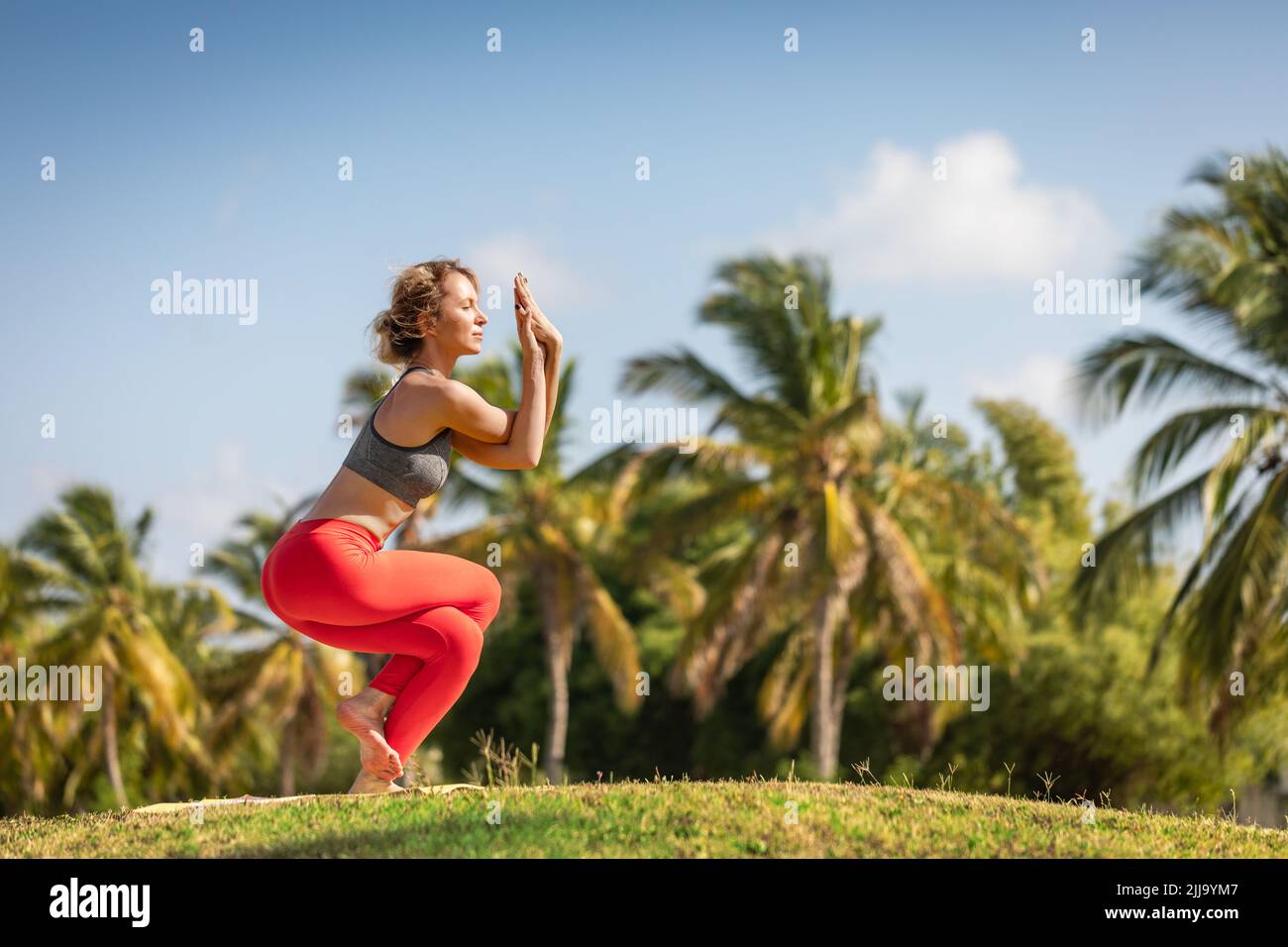 A young woman practices yoga on the ocean coast during sunrise. Stock Photo