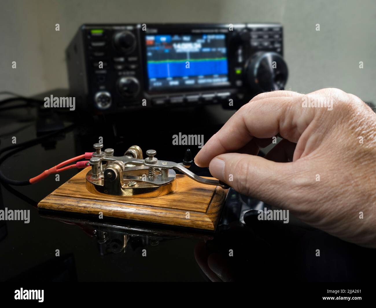Selective focus of man's hand on a telegraph key with radio defocused in background Stock Photo