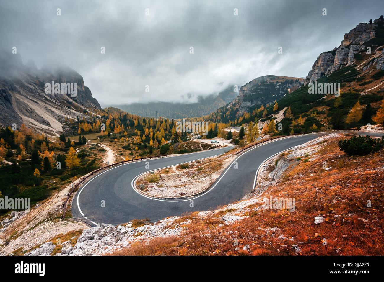 Winding mountains road leading to Three peaks of Lavaredo in Tre Cime di Lavaredo National Park in Dolomite Alps. Orange grass and lush larches forest around. Autumn in Dolomites, Italy Stock Photo