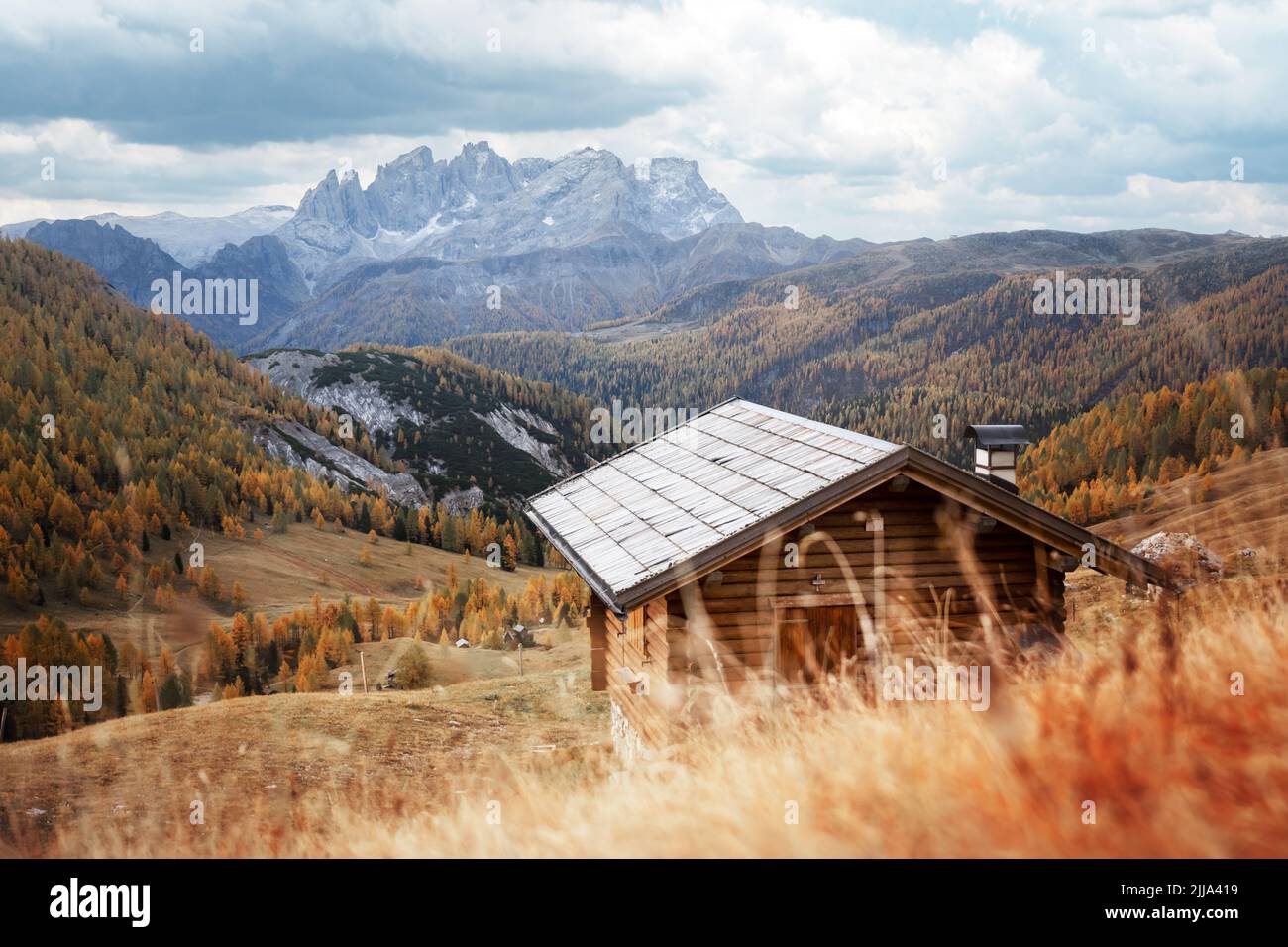 Incredible autumn view at Valfreda valley in Italian Dolomite Alps. Wooden cabin, yellow grass, orange larches forest and snowy mountains peaks on background. Dolomites, Italy. Landscape photography Stock Photo