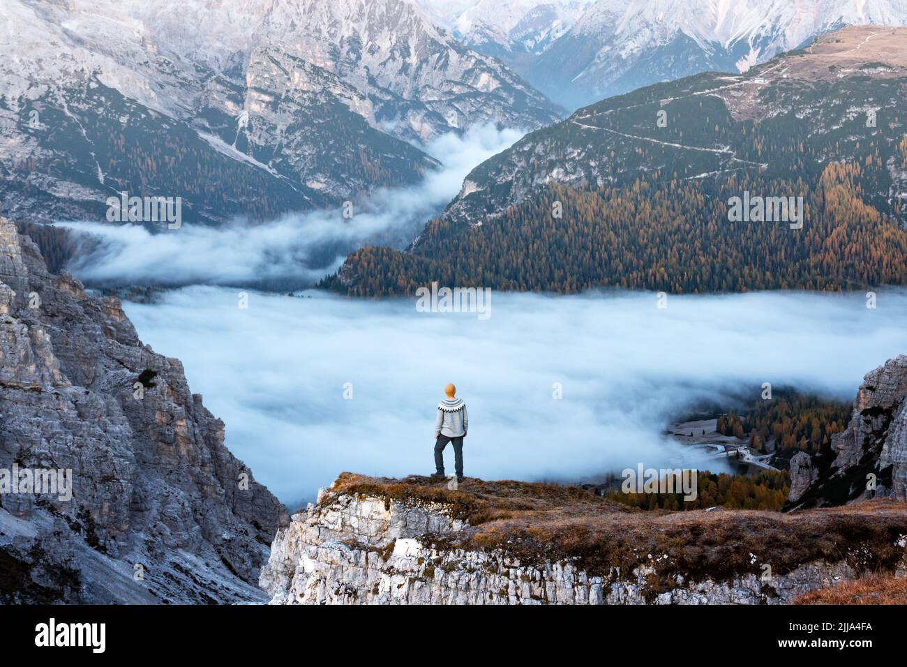 A tourist stands over the fog at the edge of a cliff in the Dolomites mountains. Location Auronzo rifugio in Tre Cime di Lavaredo National Park, Dolomites, Trentino Alto Adige, Italy Stock Photo