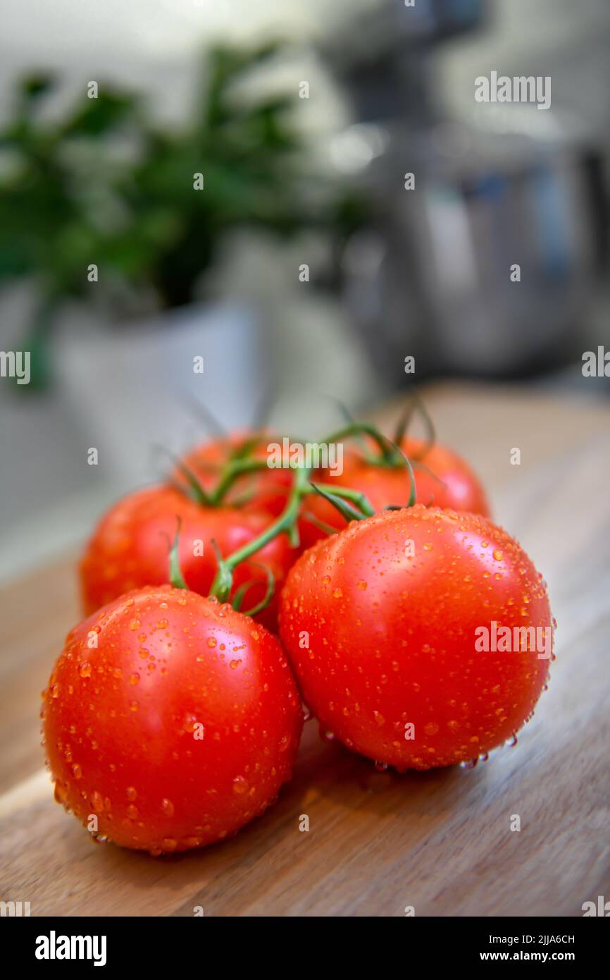 Red tomatoes on vine in kitchen - sliced and whole fresh tomato on wood cutting board - ripe Solanum lycopersicum bunch and cluster Stock Photo