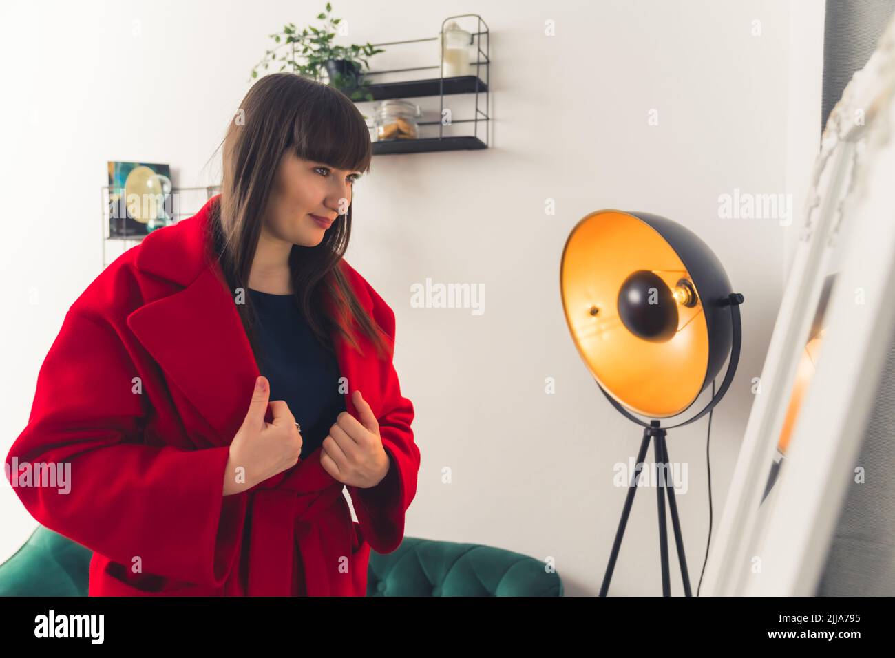 Young white brunette woman with bangs wearing a red coat looking at herself in a mirror. Indoor shot. High quality photo Stock Photo