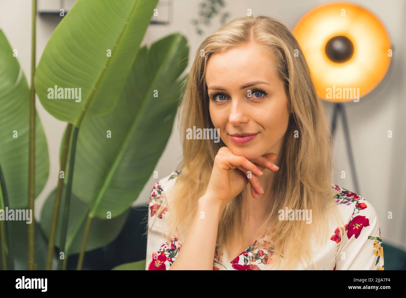 Skincare concept. Portrait of a beautiful blonde caucasian girl in her mid 20s touching her chin. Plant with big leaves in the background. High quality photo Stock Photo