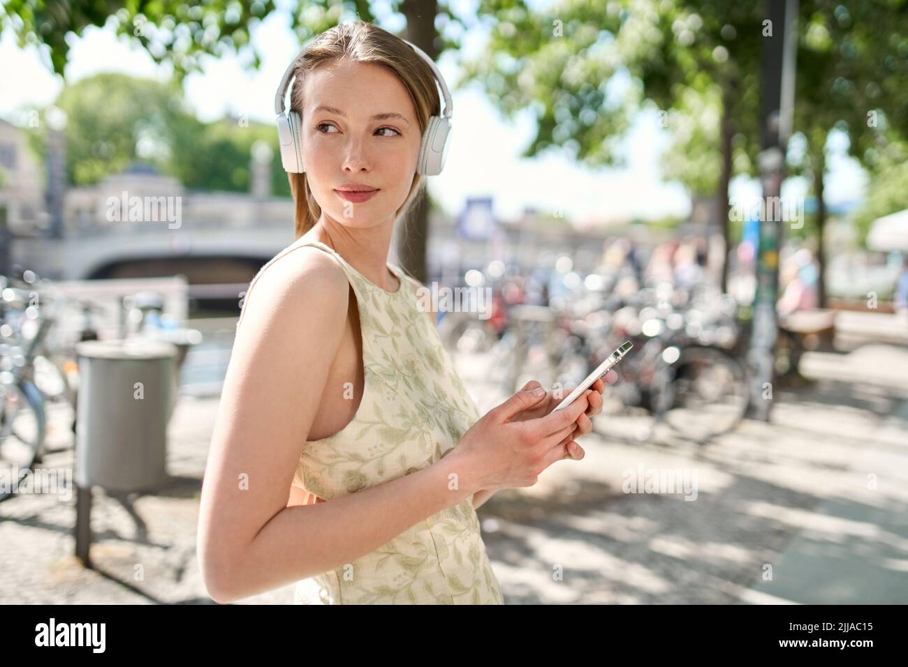 Young pretty woman standing on summer street wearing headphone using smartphone. Stock Photo