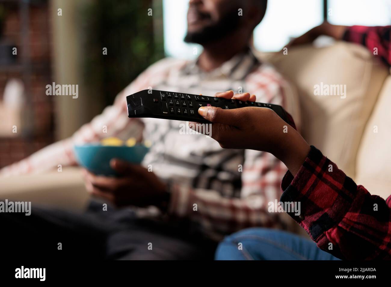 Young woman using tv remote control to switch channel program and find movie on television to watch. Eating takeaway delivery from fast food and watching film together. Close up. Stock Photo