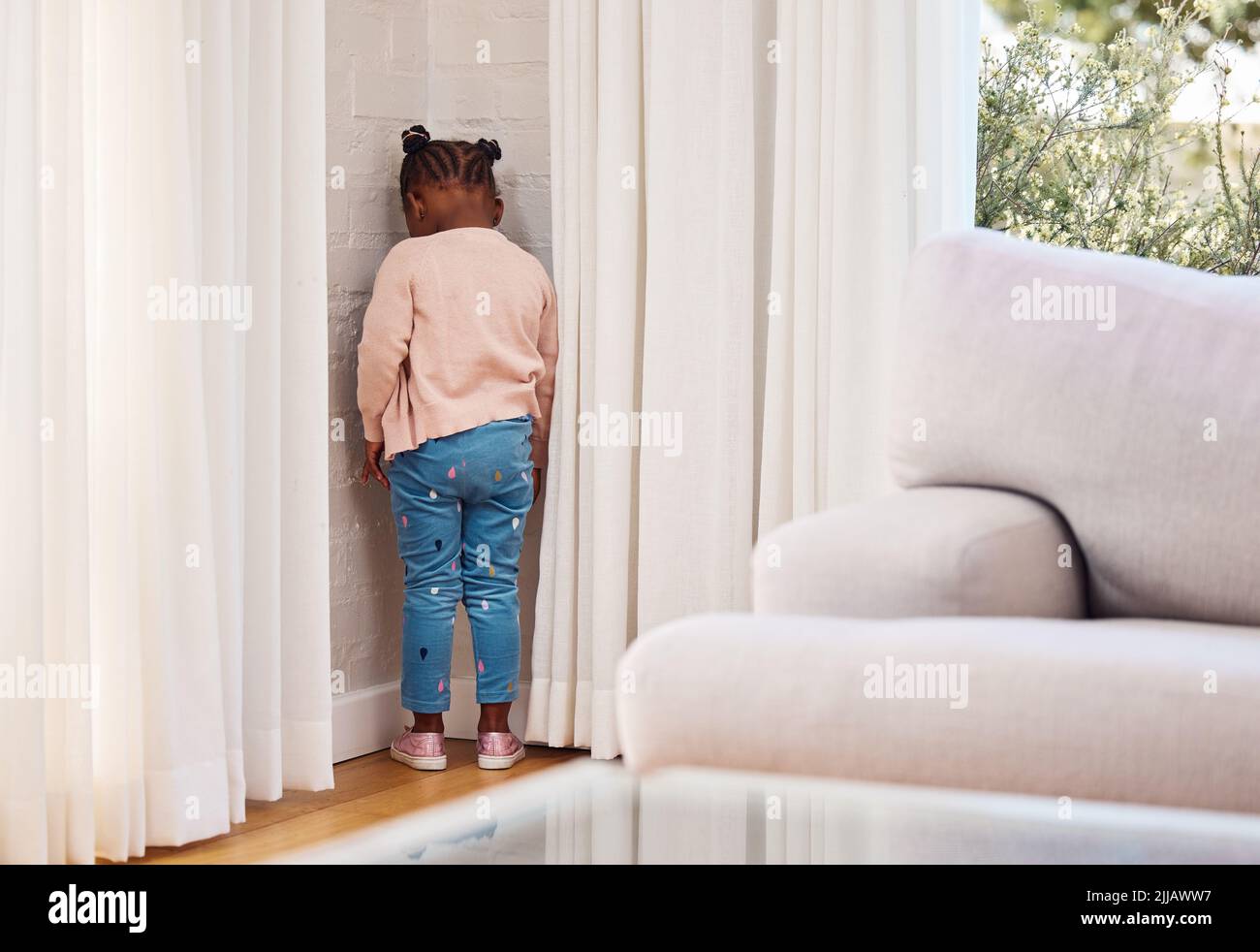 Shes been sent to timeout. a little girl standing in the corner as a punishment at home. Stock Photo