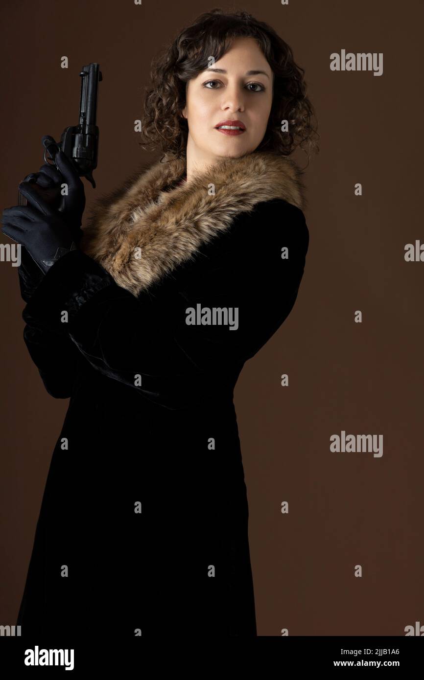 A 1920s woman wearing a velvet coat with a fur collar and holding a gun Stock Photo