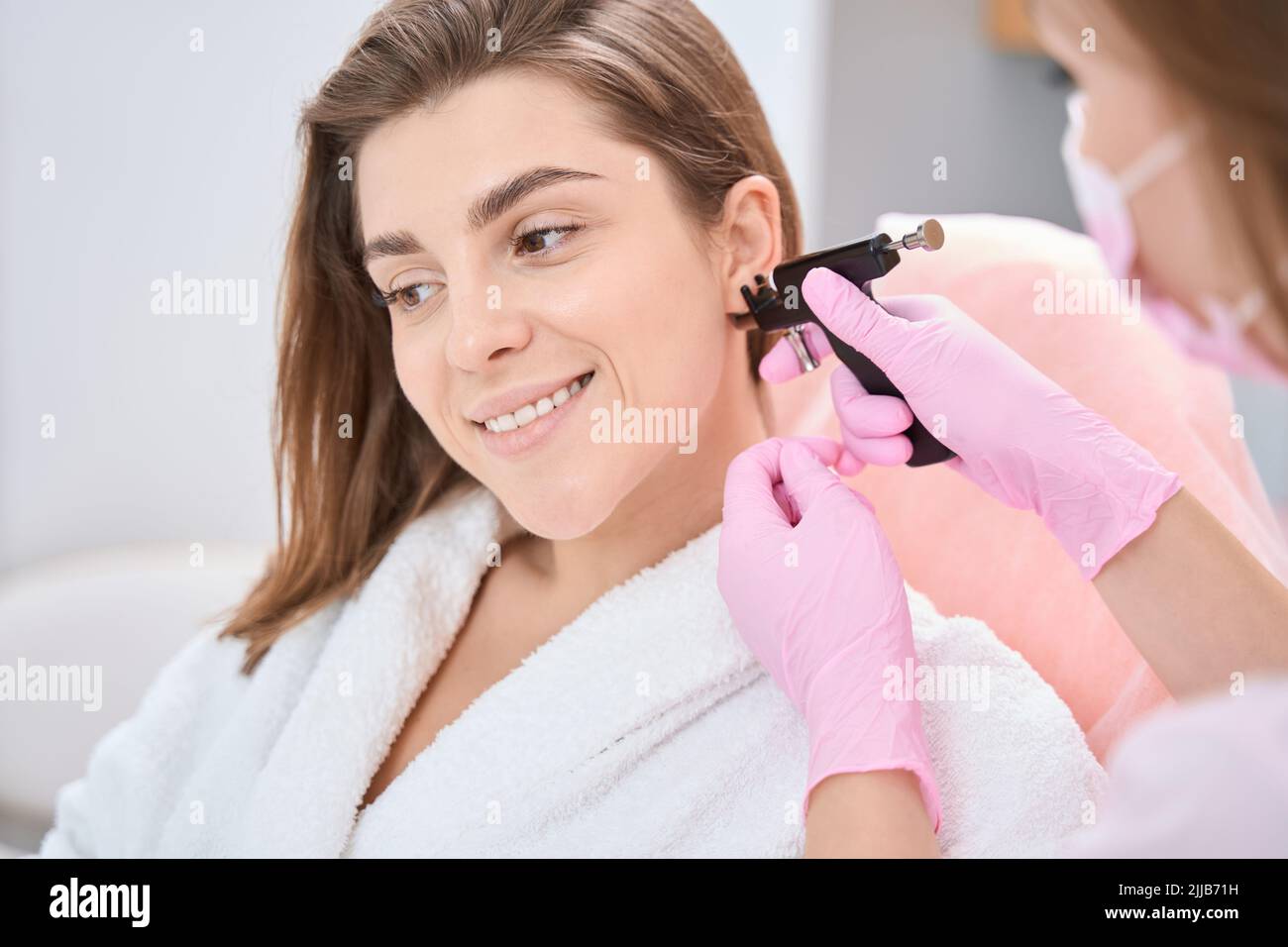 Woman is putting an ear piercing machine to her ear Stock Photo