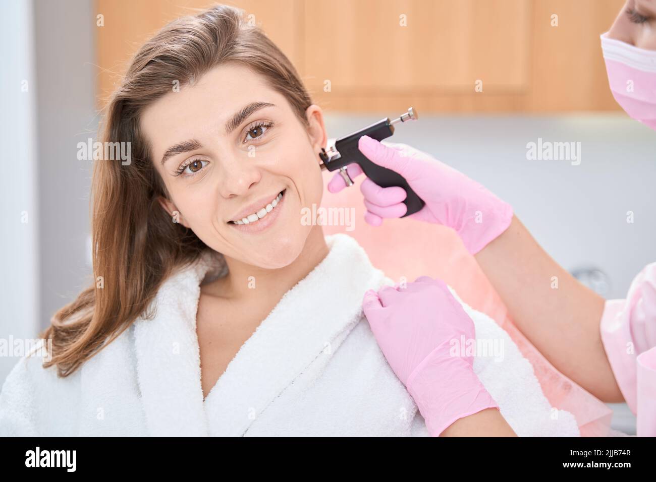 Woman is sitting in chair for ear piercing professional procedure Stock Photo