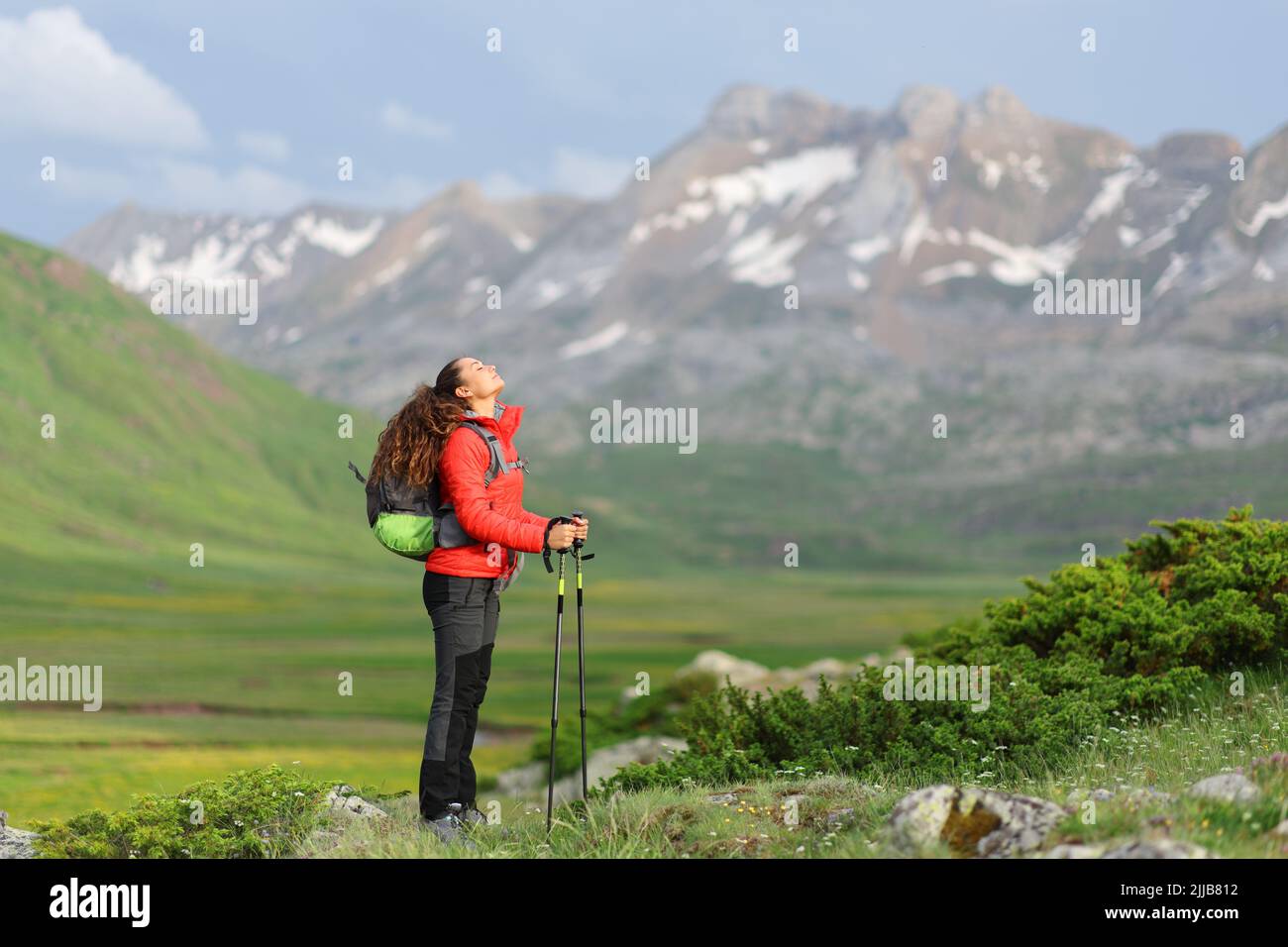 Full body portrait of a hiker in red resting and breathing fresh air in the mountain Stock Photo