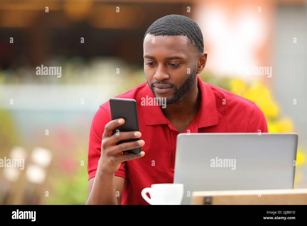 Black man in red using phone and laptop in a coffee shop terrace Stock Photo