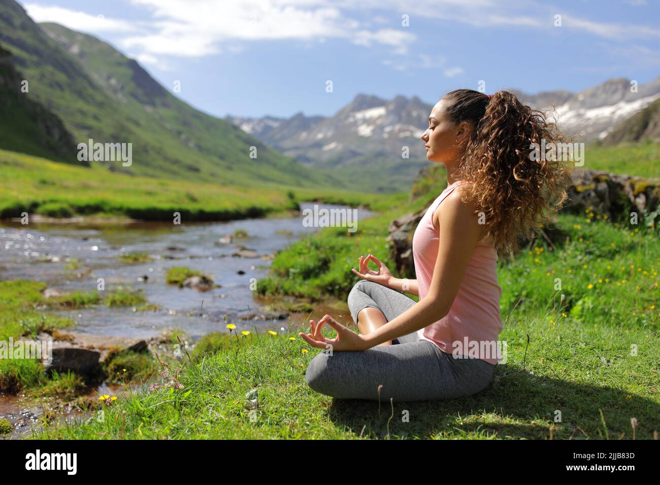 Side view full body portrait of a yogi doing yoga exercise in a riverside in a green mountain Stock Photo