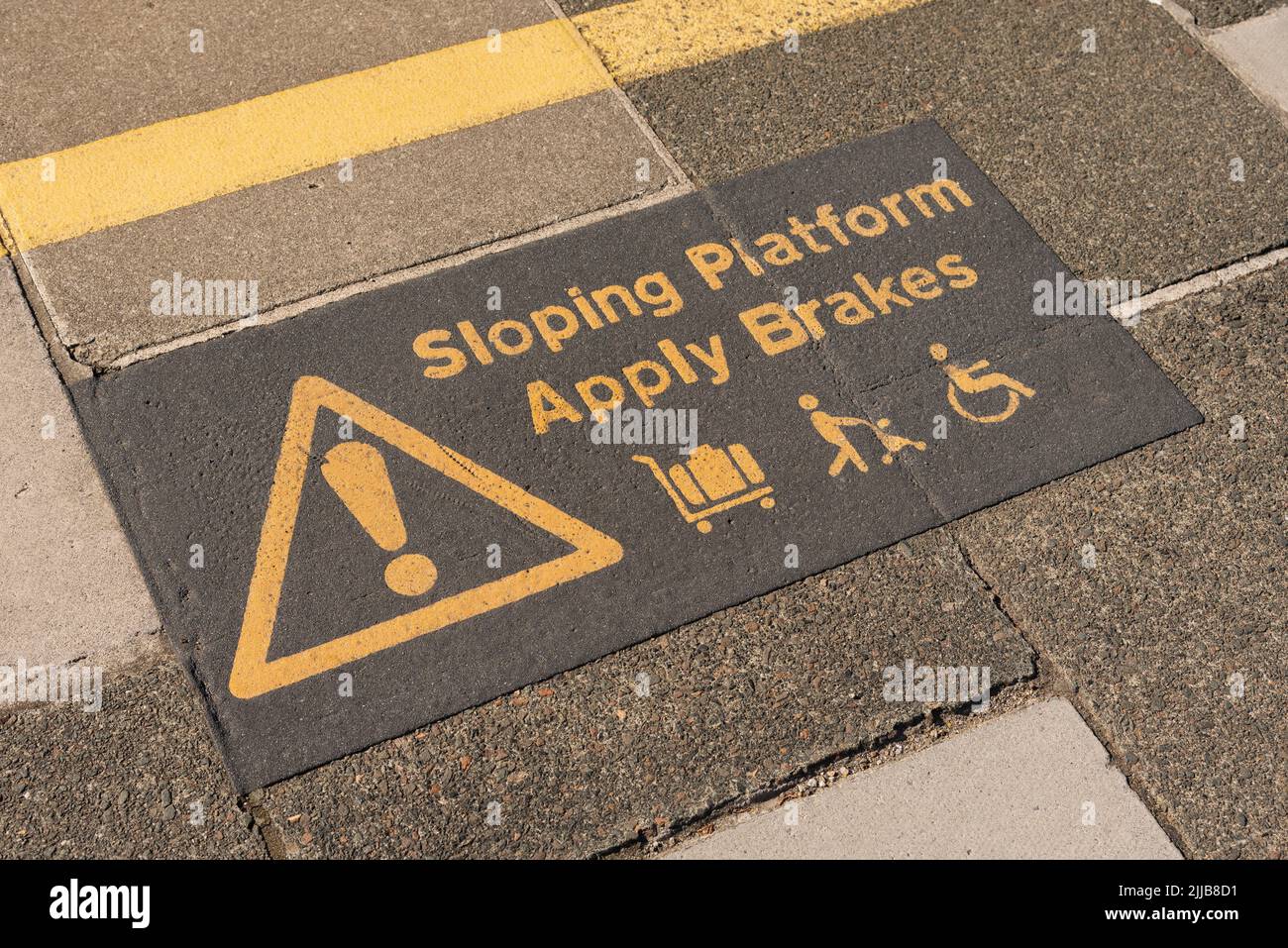St Erth, Cornwall, England, UK. 2022. Warning sign  of a sloping platform surface to passengers using wheelchairs, trolleys and pushchairs at St Erth Stock Photo